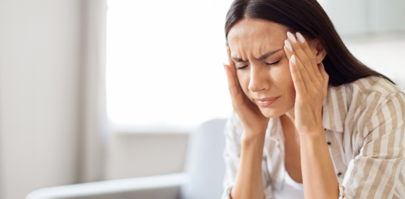 A young woman with her hands either side of her head, looking in pain