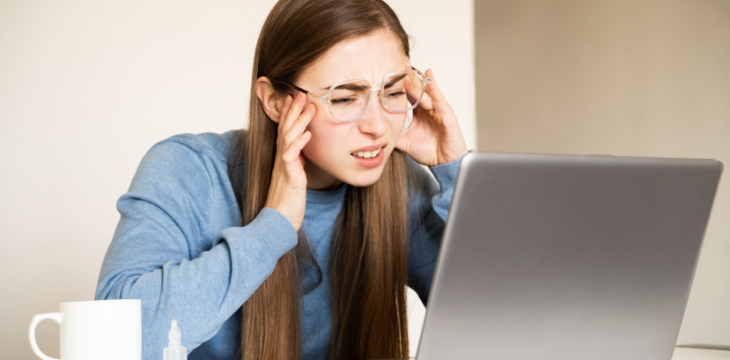 A young woman wearing glasses, squinting at her computer screen