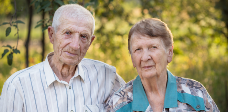 An elderly couple standing outside together looking towards the camera