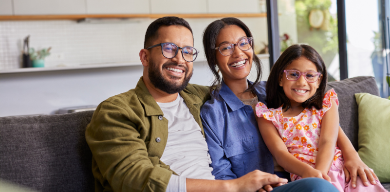 A family sat on their sofa at home, all wearing spectacles