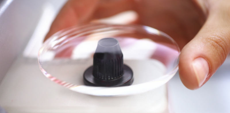 A person carefully holding a prescription lens under a measurement device in an optical lab