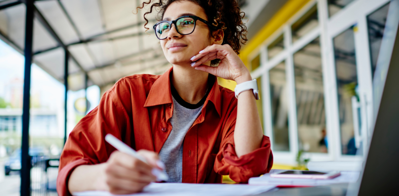 Young woman with glasses looking out at the distance while working outside